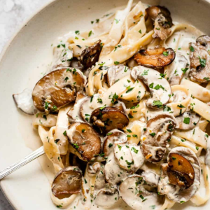 "A plate of creamy pasta topped with fresh herbs, grated cheese, and a rich sauce, served in a beautifully arranged dish."