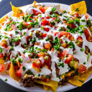 A plate of crispy nachos topped with melted cheese, jalapeños, sour cream, and a sprinkle of fresh cilantro, ready to be enjoyed."