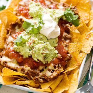 "A plate of crispy nachos topped with melted cheese, jalapeños, sour cream, and a sprinkle of fresh cilantro, ready to be enjoyed."