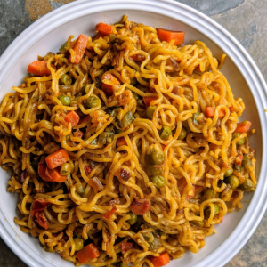 "A bowl of steaming noodles garnished with fresh vegetables, herbs, and a flavorful sauce, served as a delicious and comforting dish."
