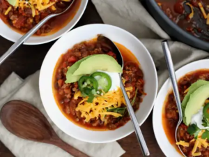 "A hearty bowl of award-winning chili, filled with tender meat, beans, and a rich blend of spices, topped with shredded cheese and fresh herbs."