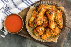 "Golden, oven-crisp chicken wings served with a side of dipping sauce, garnished with fresh herbs."